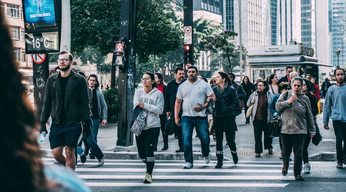A diverse group of people crossing a street in a bustling city setting with skyscrapers
