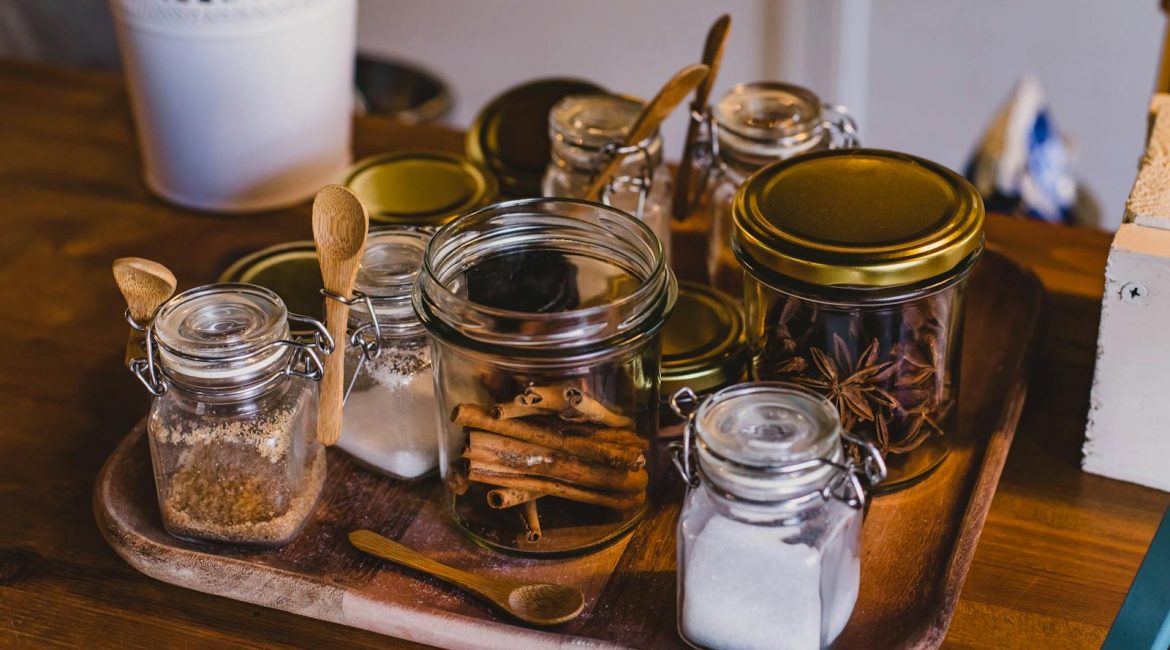 An arrangement of spice jars and cinnamon sticks on a wooden tray in a cosy kitchen setting