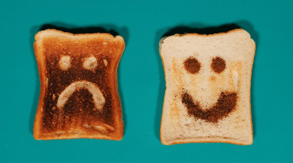 Two slices of toast with happy and sad faces on a teal background