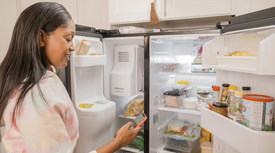 A woman stands at the open fridge in a kitchen, checking her phone