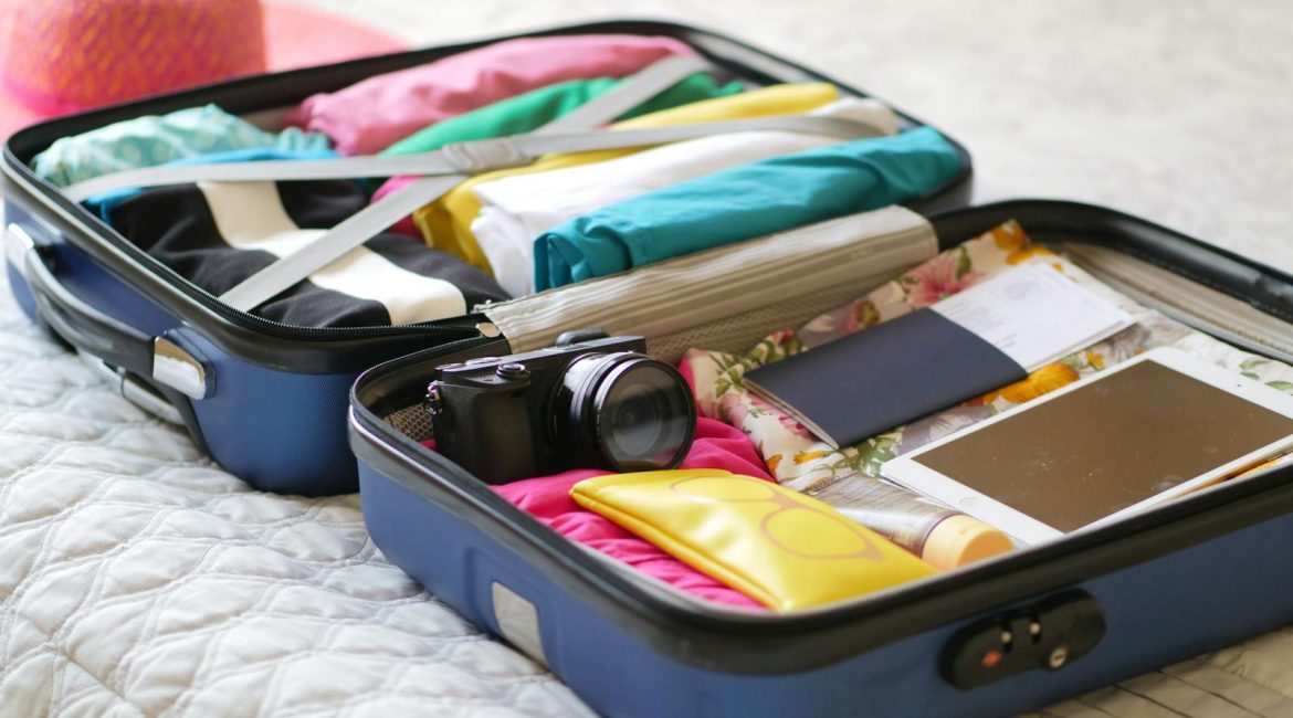 Open suitcase with camera, clothes, and passport, ready for a summer vacation